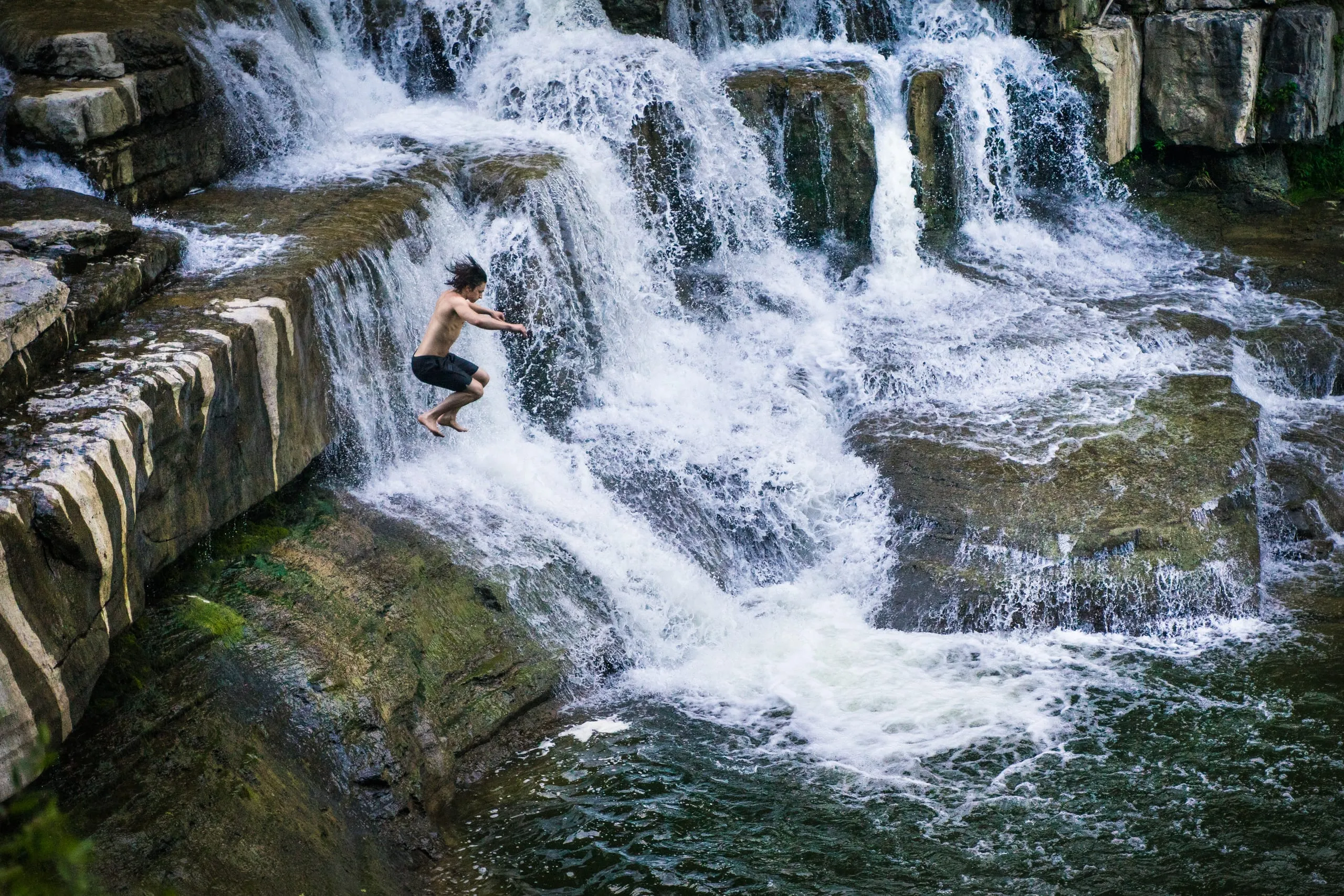 A swimmer leaping from a rock ledge beside a cascading waterfall, Finger Lakes, New York