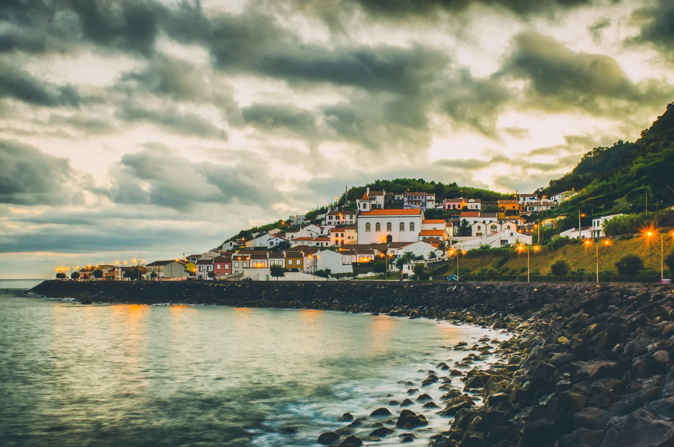 Azorean coastal village glowing at dusk above a wet volcanic shore